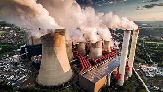 A bird's eye view of a power plant billowing emissions by burning fossil fuels.