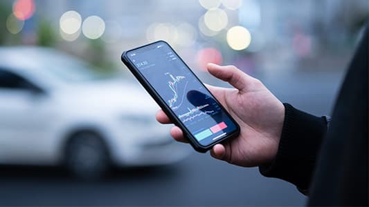 A man holding his phone, the phone is showing a share prices unstable volatility.