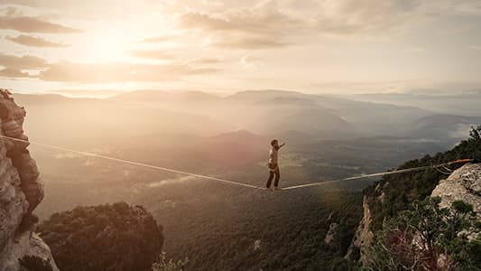 A tight rope walker taking big risk as he balances over a steep cliff.
