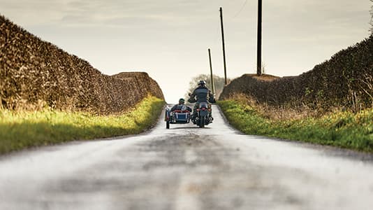 Two people riding a motorbike through the countryside in the UK.