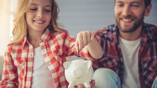 A father teaching his daughter how to save money through the use of a piggy bank.