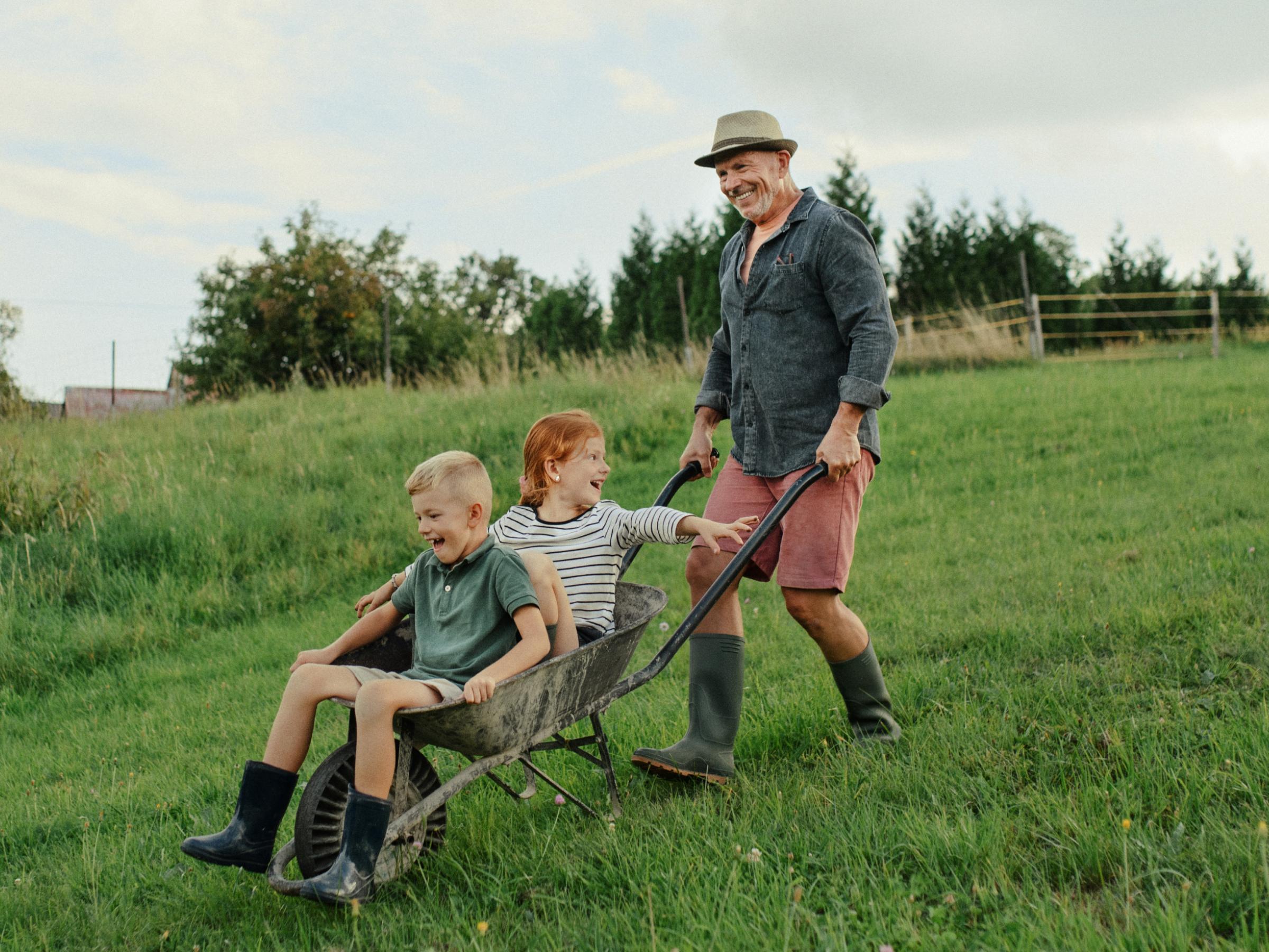 A Kiwi farmer supporting the weight of his grandchildren in a wheelbarrow.